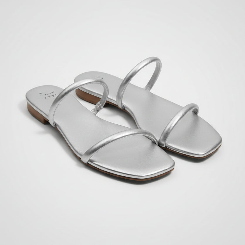 Silver sandals on a cardboard surface with a tag attached.
