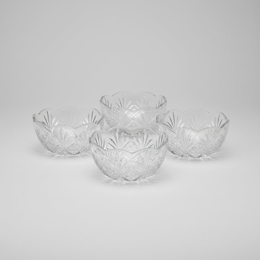 Four clear glass bowls with intricate patterns on a wooden surface.