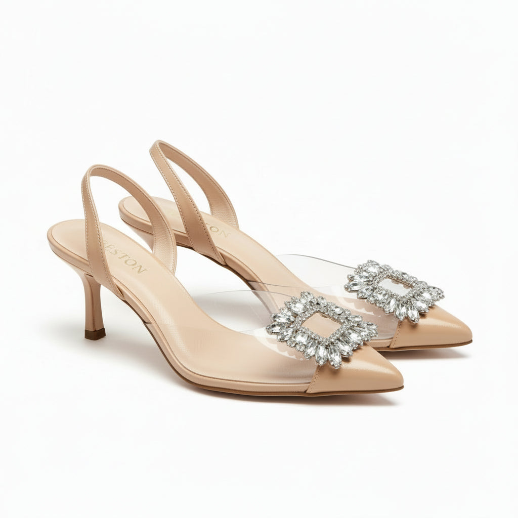 White high-heeled shoes with a decorative brooch on a cardboard surface.